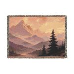 Woven blanket with mountain and tree landscape design on a white background